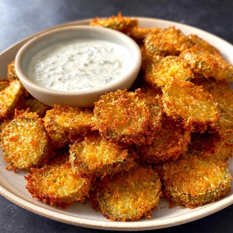 A bowl of fried pickles with a dipping sauce.