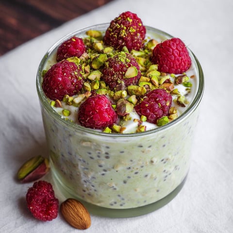 A glass of pistachio overnight oats with raspberries on top.